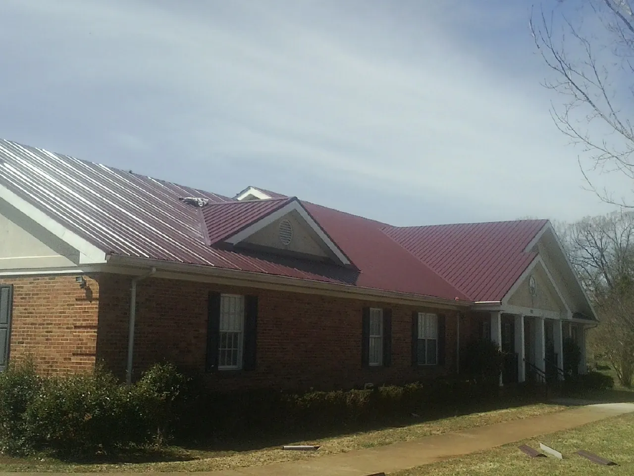 Red metal roof with gabled entries on a long brick building, from a Hail Damage Roof Repair job in Bernardston