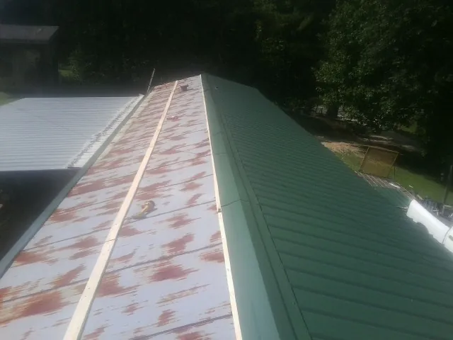 Old rusted panels beside newly installed green metal roofing — Wind Damage Roof Repair by Roofing Brothers in Bernardston
