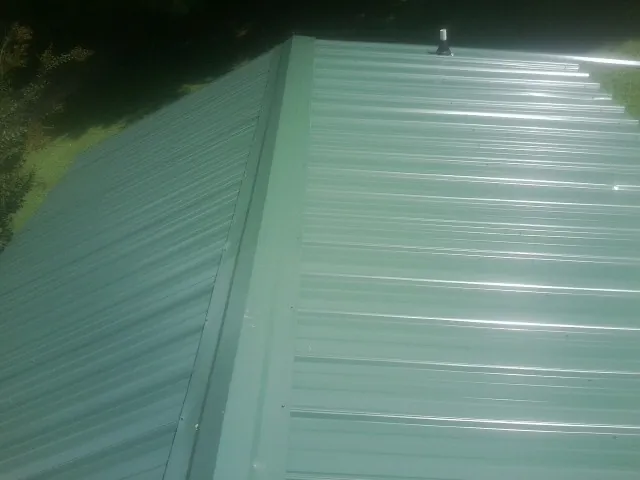 New green metal panels meeting at the ridge of a roof — Flat Roof Repair work by our crew in Bernardston