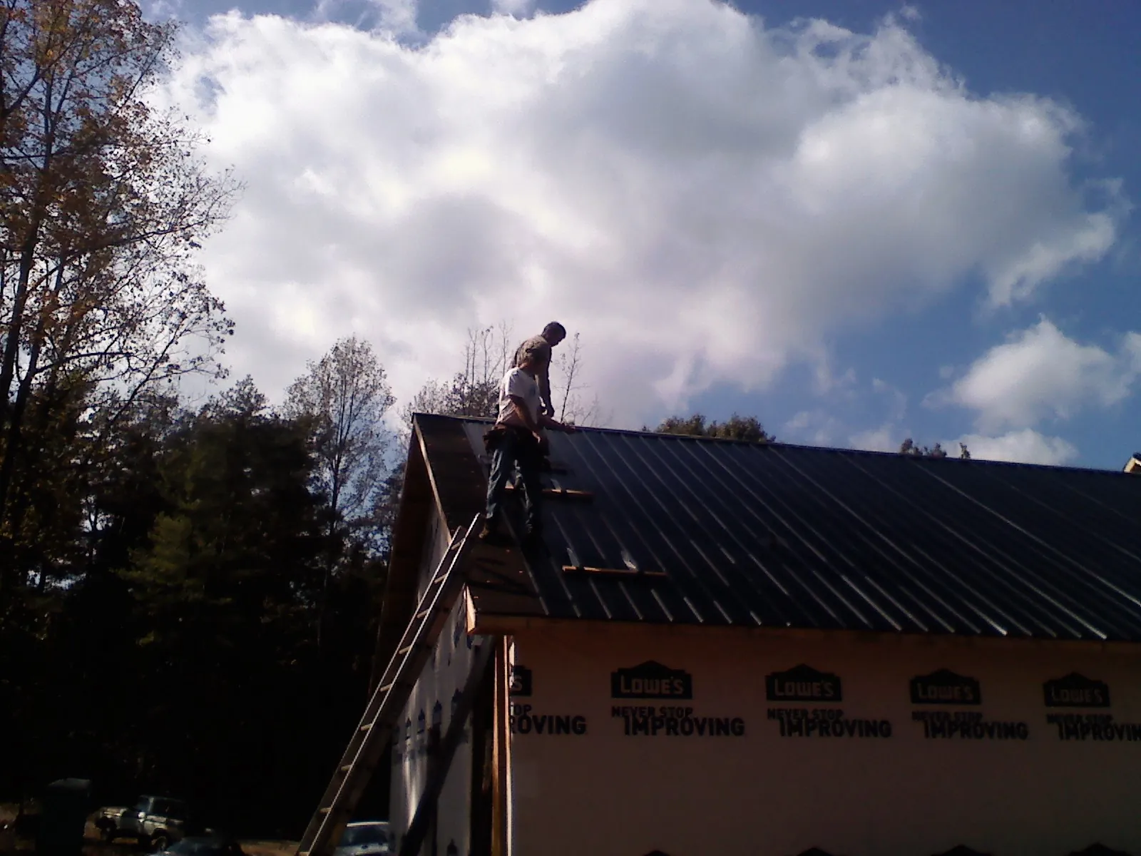 Roofer fastening dark metal panels high against a cloudy sky, from a Roof Inspection job in Bernardston