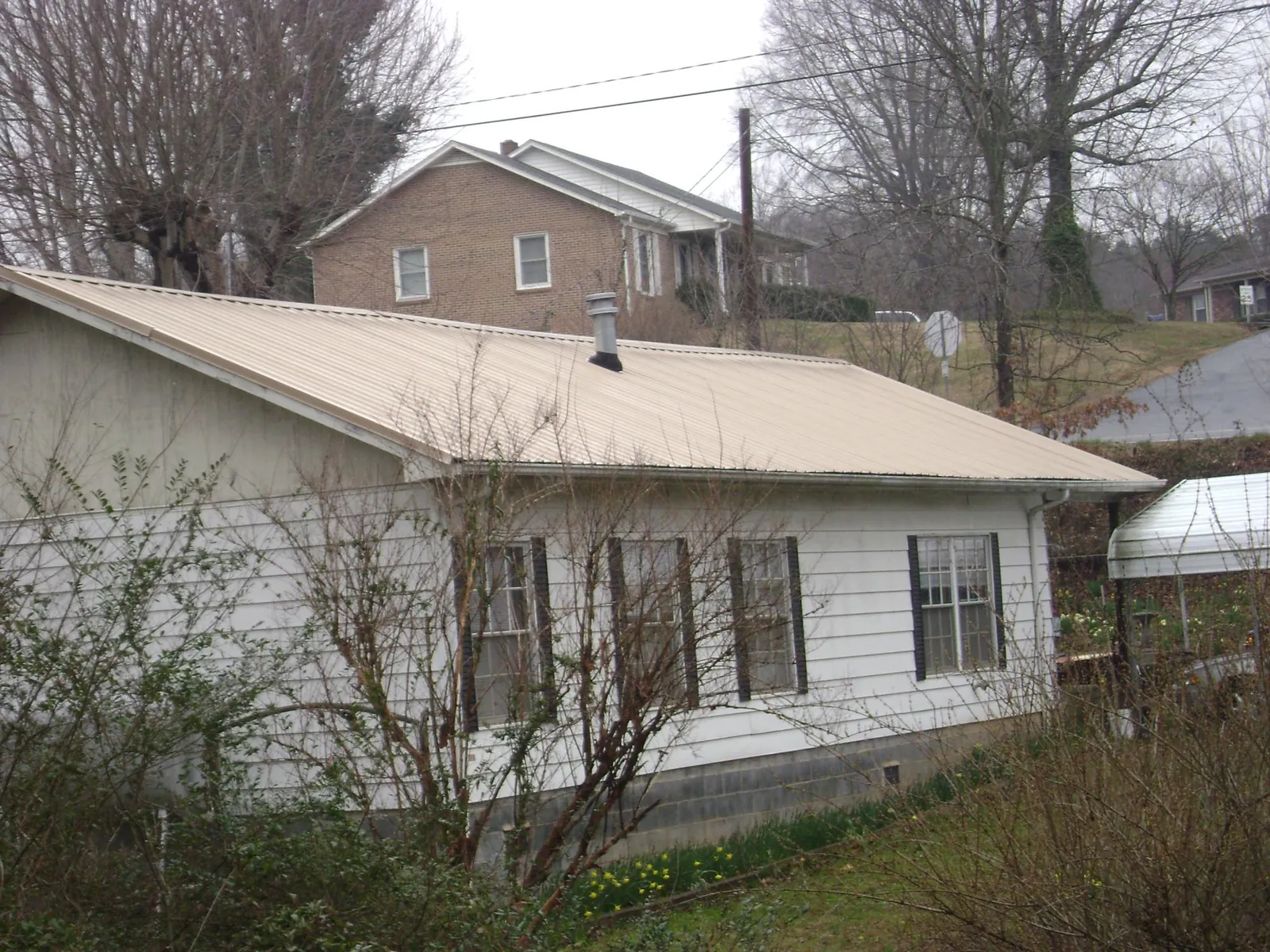 Tan metal roof on a white sided house set into a hillside — Commercial Roofing by Roofing Brothers in Bernardston
